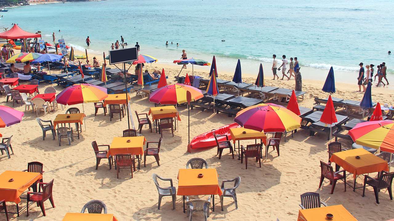 A busy beach with lots of red and yellow umbrellas, tables, chairs, and people