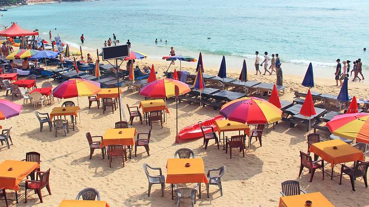A busy beach with lots of red and yellow umbrellas, tables, chairs, and people