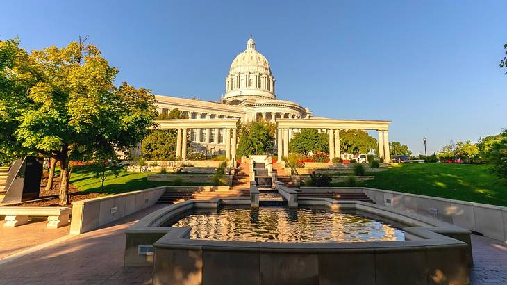 A pond with water surrounded by greenery with a capitol building behind it