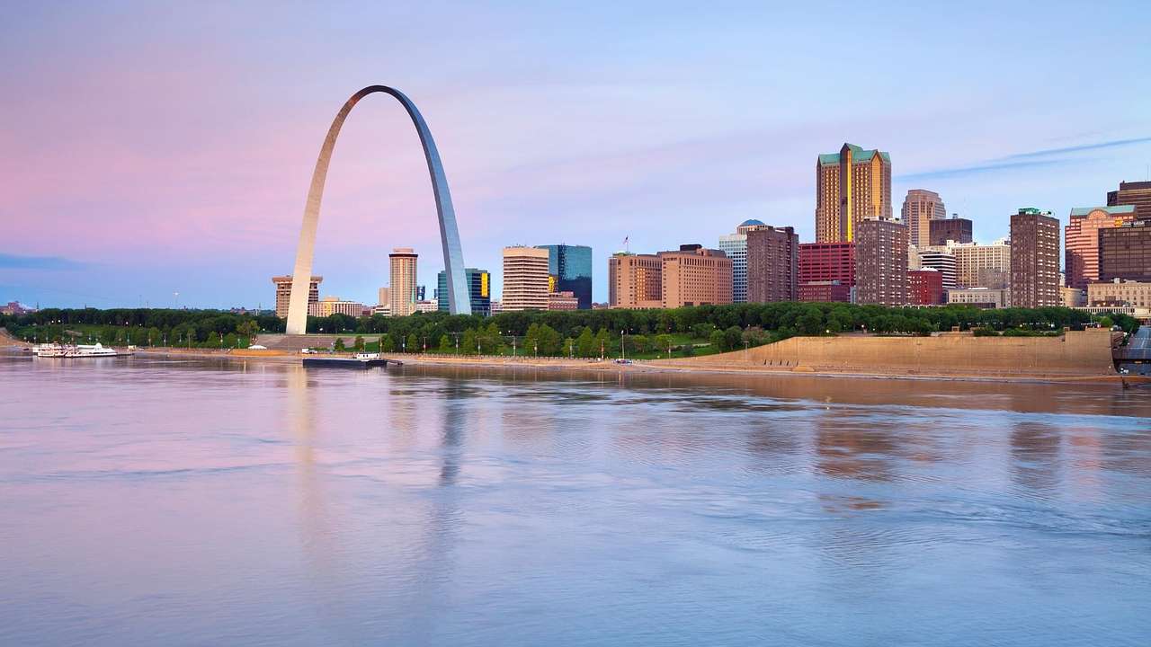 A skyline of tall skyscrapers and a huge arch monument overlooking a river