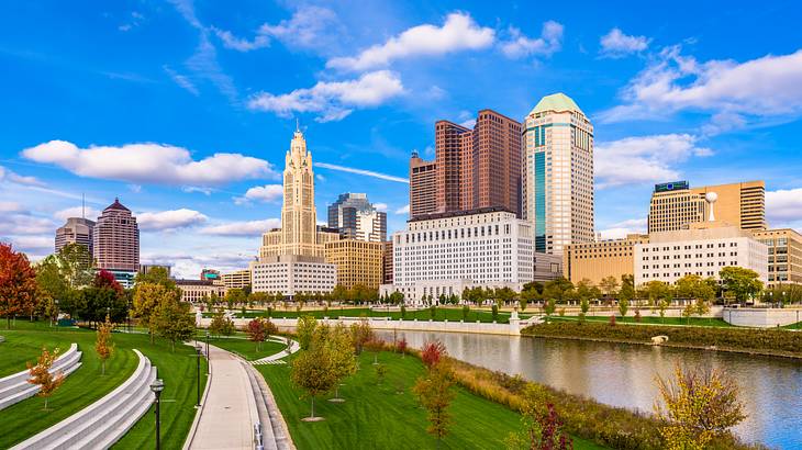 A riverwalk surrounded by greenery and various buildings along a riverbank A riverwalk surrounded by greenery and various buildings along a riverbank