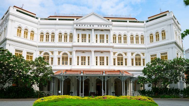 The exterior of a grand hotel with trees and greenery in front