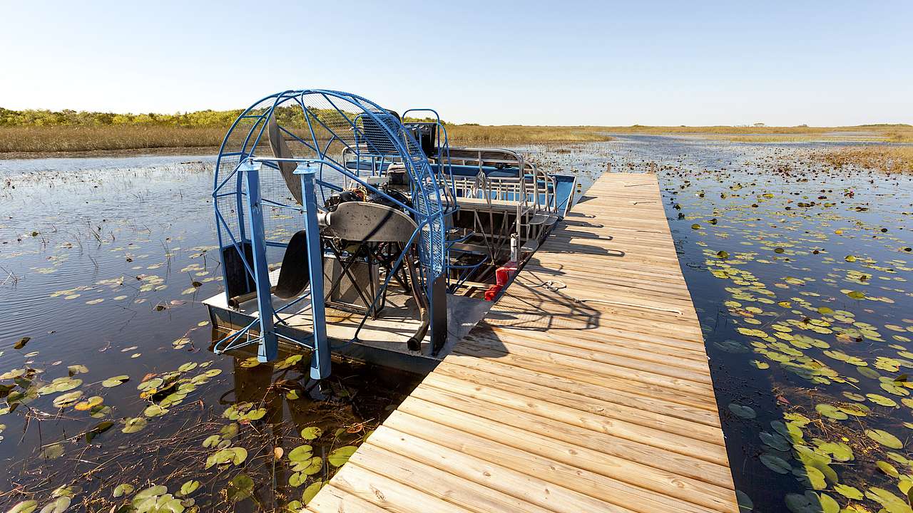 A boardwalk stretching into a swamp with an airboat next to it on a sunny day