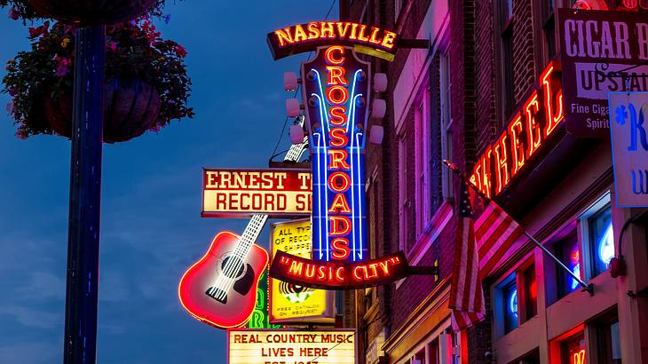 Neon lights and signs against buildings, one saying "Nashville Crossroads Music City"
