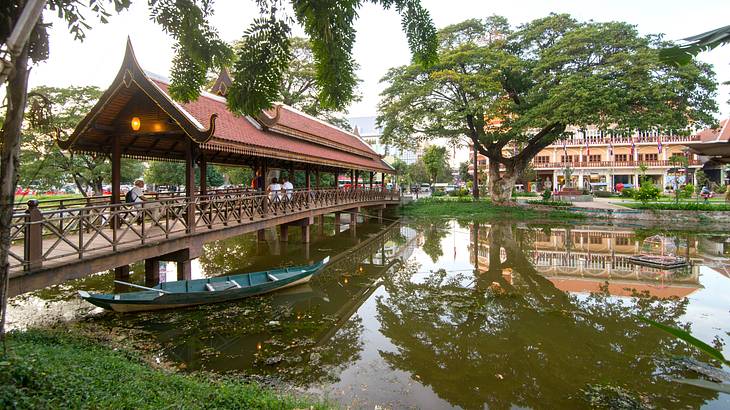 A bridge over water with a boat on the left, and buildings and trees behind