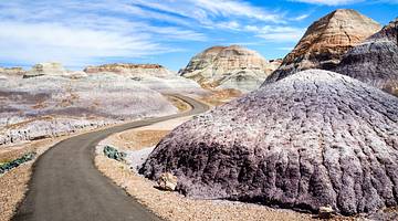 An asphalt road through a desert landscape surrounded by arid hills on a sunny day
