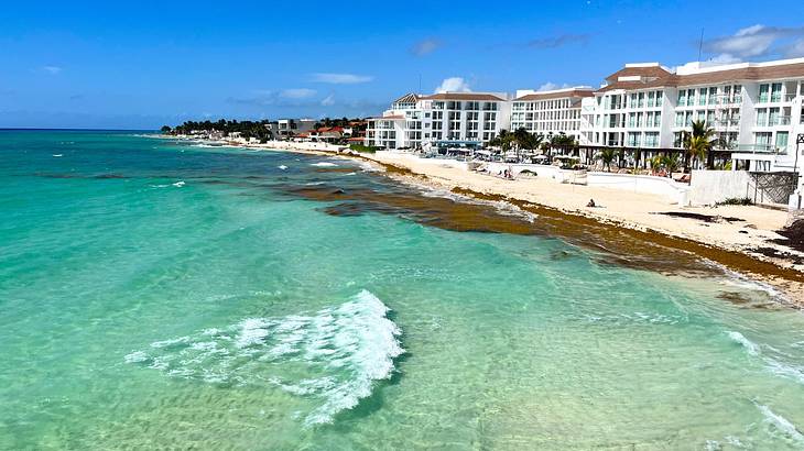 Blue crystal-clear water gently lapping a white sandy beach with grand hotels