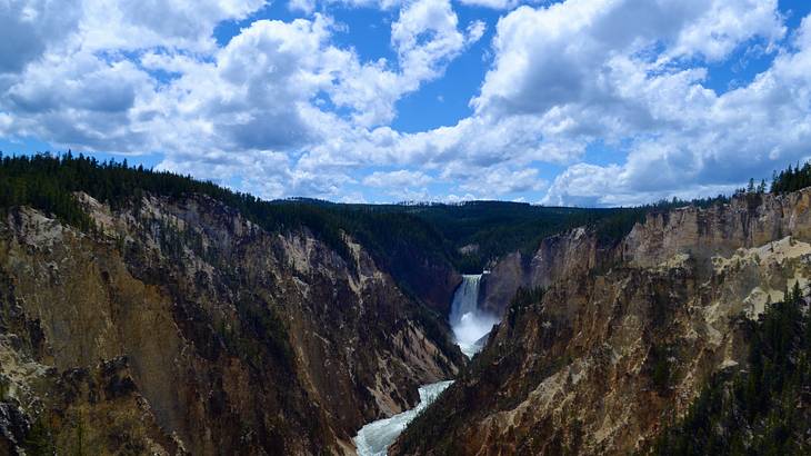 A grand canyon with a waterfall winding through and a partly cloudy sky above