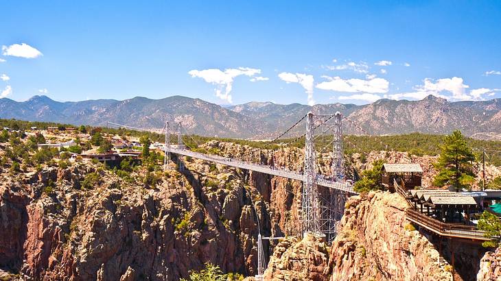 A white suspension bridge over rugged terrain, against hazy mountains
