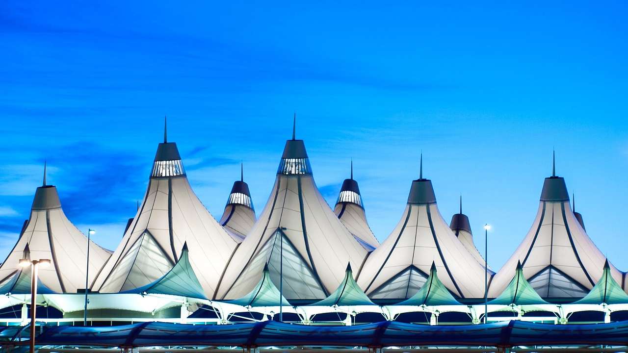 A modern airport building with white spiky roofs under a blue sky