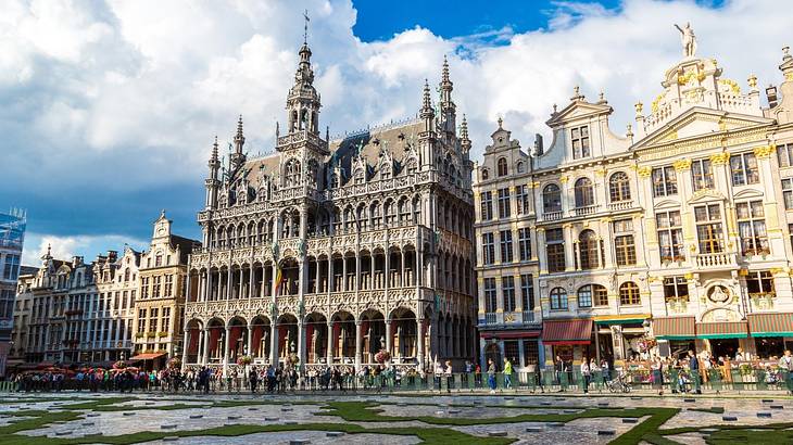 A Neo-Gothic and Baroque palace with grass, a street, and tourists in front of it