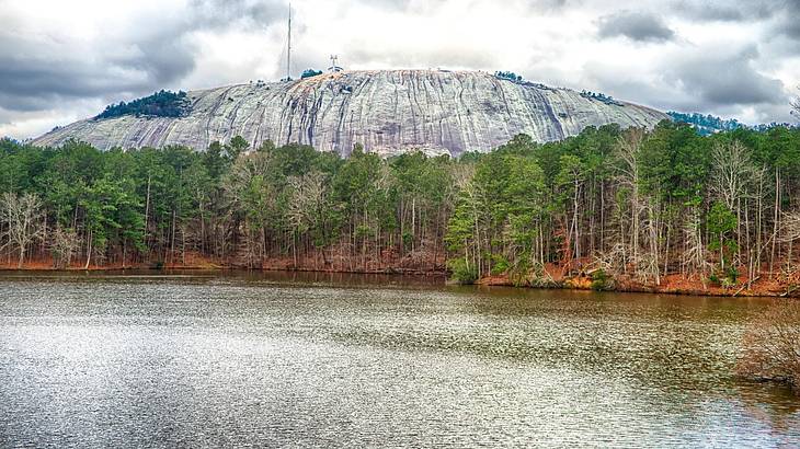 A mountain with trees and a lake in front of it under a cloudy sky