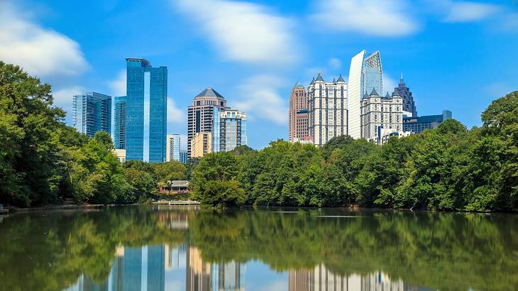 Skyscrapers behind a lake with reflections in the water and green trees around it