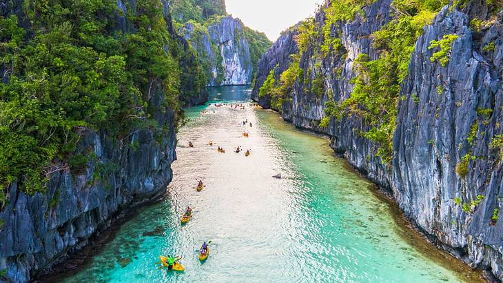 Water flowing between rocky greenery-covered cliffs with people kayaking on it