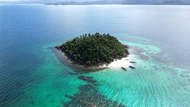 A lush green island with a white beach from above, surrounded by clear blue water