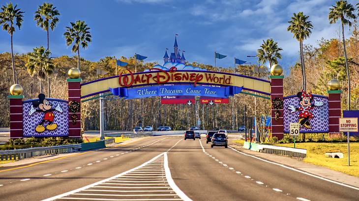 A wide road with a sign with cartoon characters on each side and greenery at the back