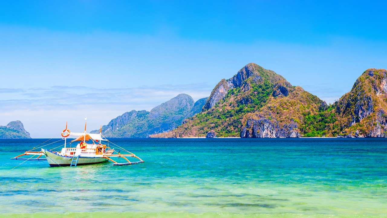 A boat on turquoise water next to a mountain covered with greenery