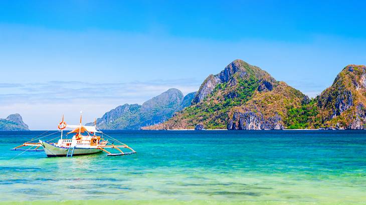 A boat on turquoise water next to a mountain covered with greenery