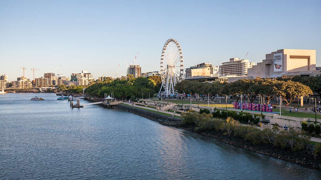 A park with a giant wheel, a large water body in front, and buildings around the back