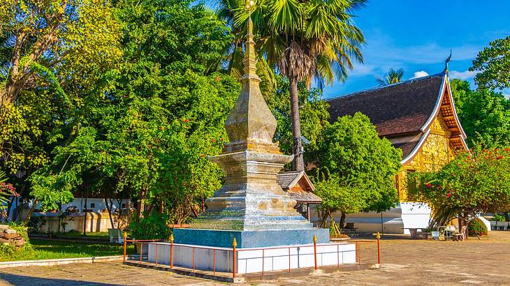 A small temple next to a statue surrounded by lush green trees