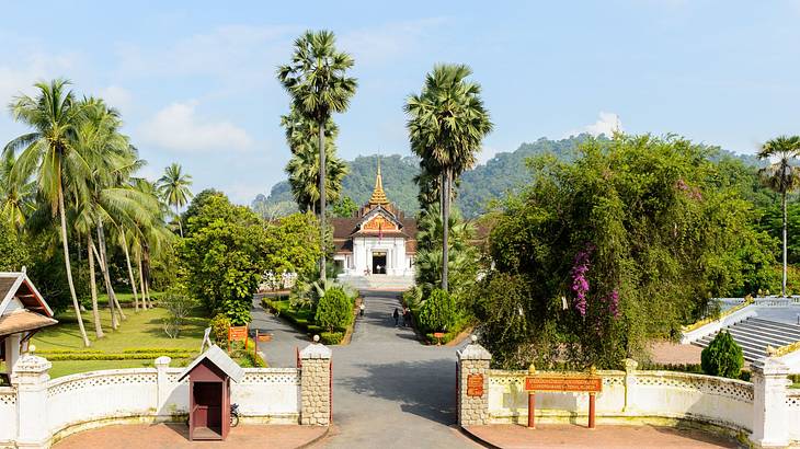 A gate leading to a small palace-style building surrounded by green trees