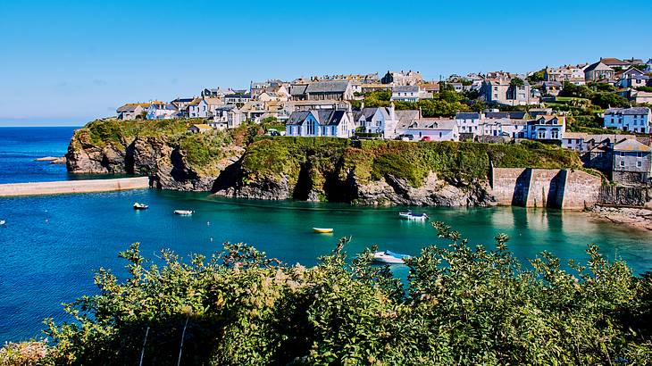 A town with houses built on a green cliff, with boats on the water below