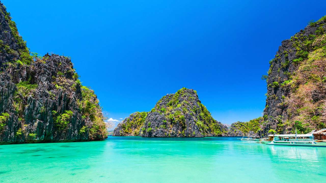 Turquoise water next to hills covered with greenery under a clear blue sky