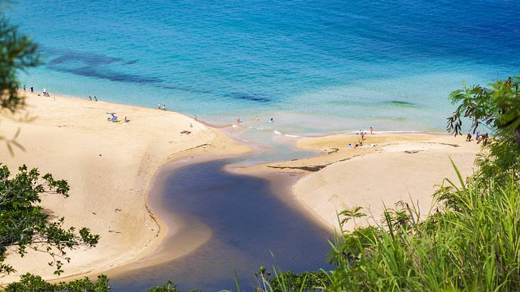 A beach separated by a stream of water flowing into the clear, blue sea