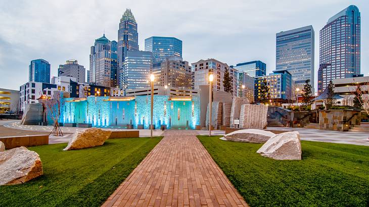 A walkway lined by grass with light posts and buildings in the distance