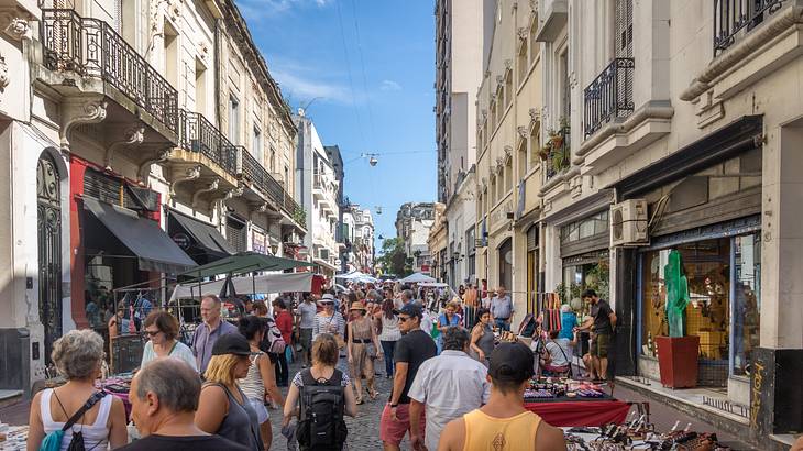 Historic buildings line a busy market street full of people walking and tables