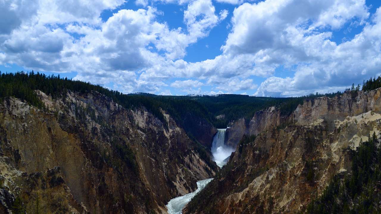 A vast canyon with a waterfall winding through and a partly cloudy sky above