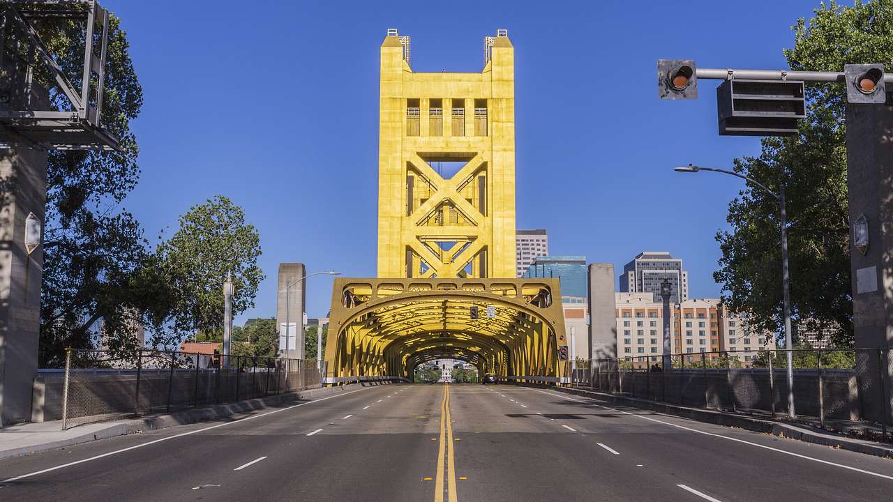 A road leading to a yellow steel bridge archway with skyscrapers in the background