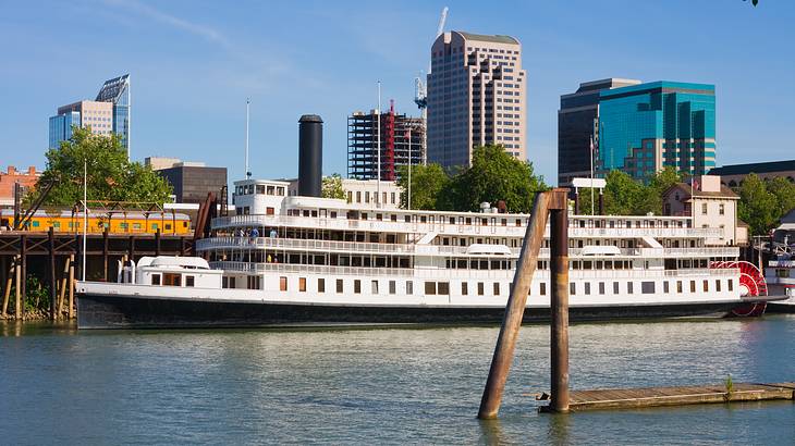 A large white boat in a river with buildings and skyscrapers at the back