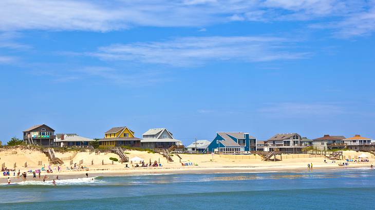 A sandy beach with houses and a few people next to the ocean on a partly cloudy day