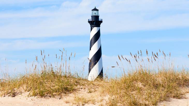 A tall lighthouse with black and white stripes surrounded by beach dunes