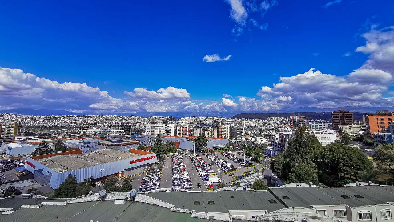 An urban setting with many buildings, cars, and trees under a blue sky with clouds