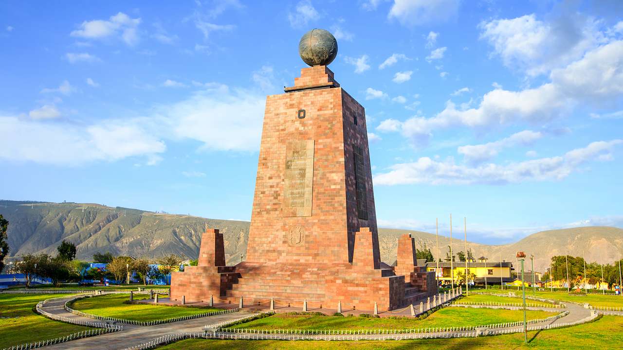 A monument with a globe on top surrounded by greenery under a partly cloudy sky