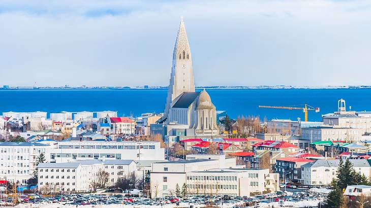 A church nestled among buildings and houses with the blue sea in the background