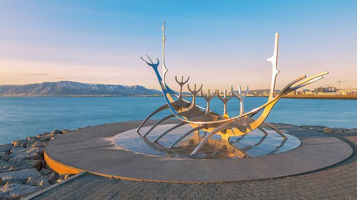 A steel sculpture of a ship with curving lines and a surface reflecting the sunlight