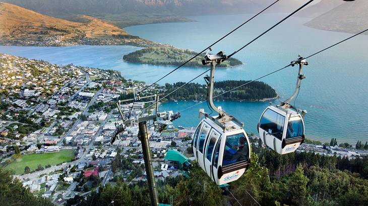 Cable cars above a town of multiple houses beside the lake and mountains