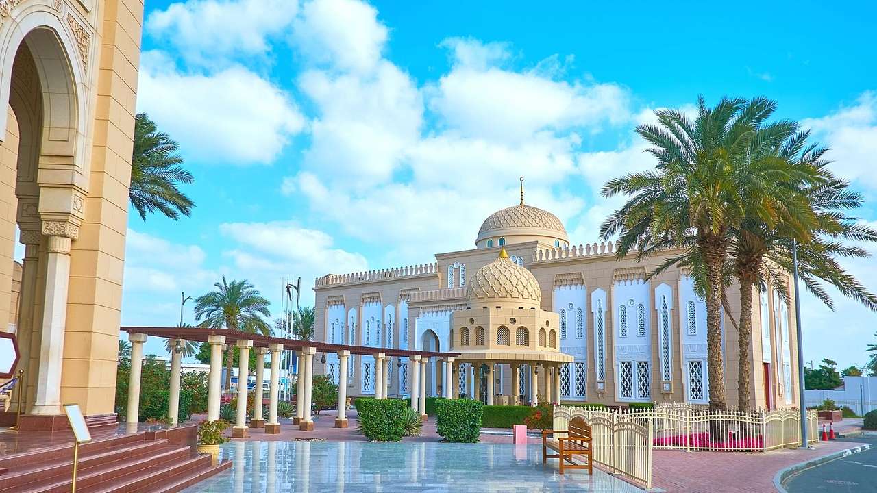 A mosque next to a garden with columns, a small pool, and palm trees