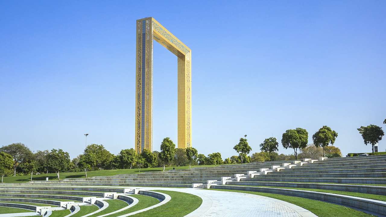 A large gold frame next to steps in the grass and trees under a blue sky