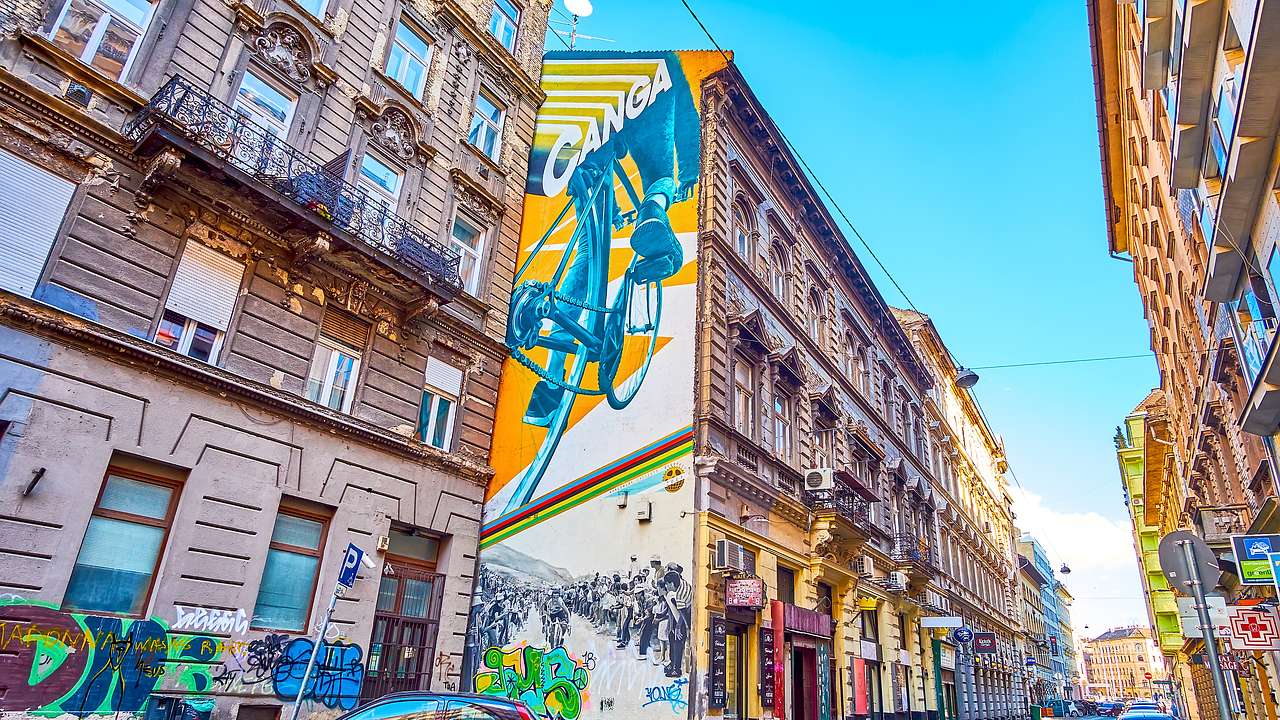 Murals on old, colorful buildings along a street with cars parked on the side