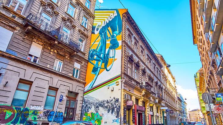 Murals on old, colorful buildings along a street with cars parked on the side