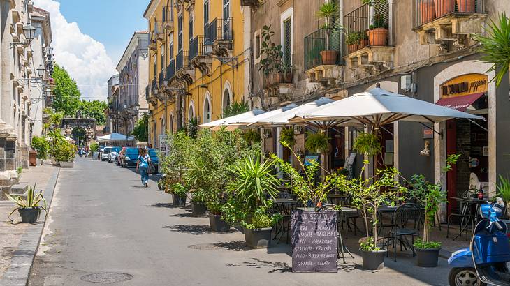 A picturesque street with colourful buildings, plants, and sun umbrellas