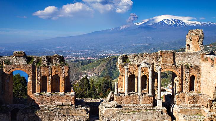 Ruins with columns and a snow-capped green mountain in the background