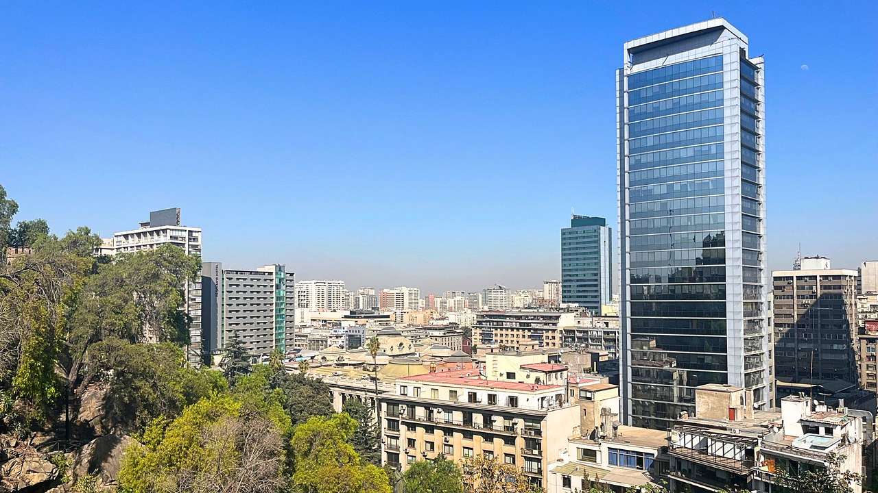 A city skyline with a few tall glass buildings, shorter buildings, and green trees