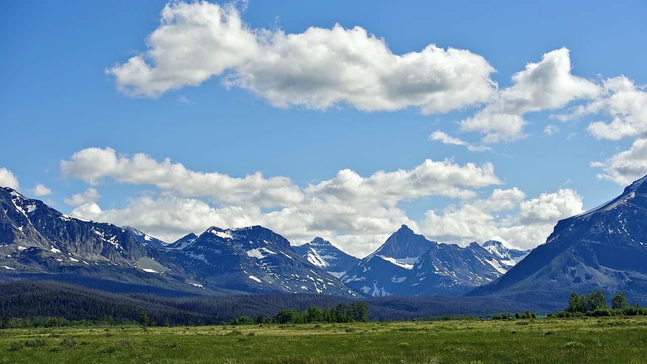 A green field at the base of rocky mountains with patches of snow