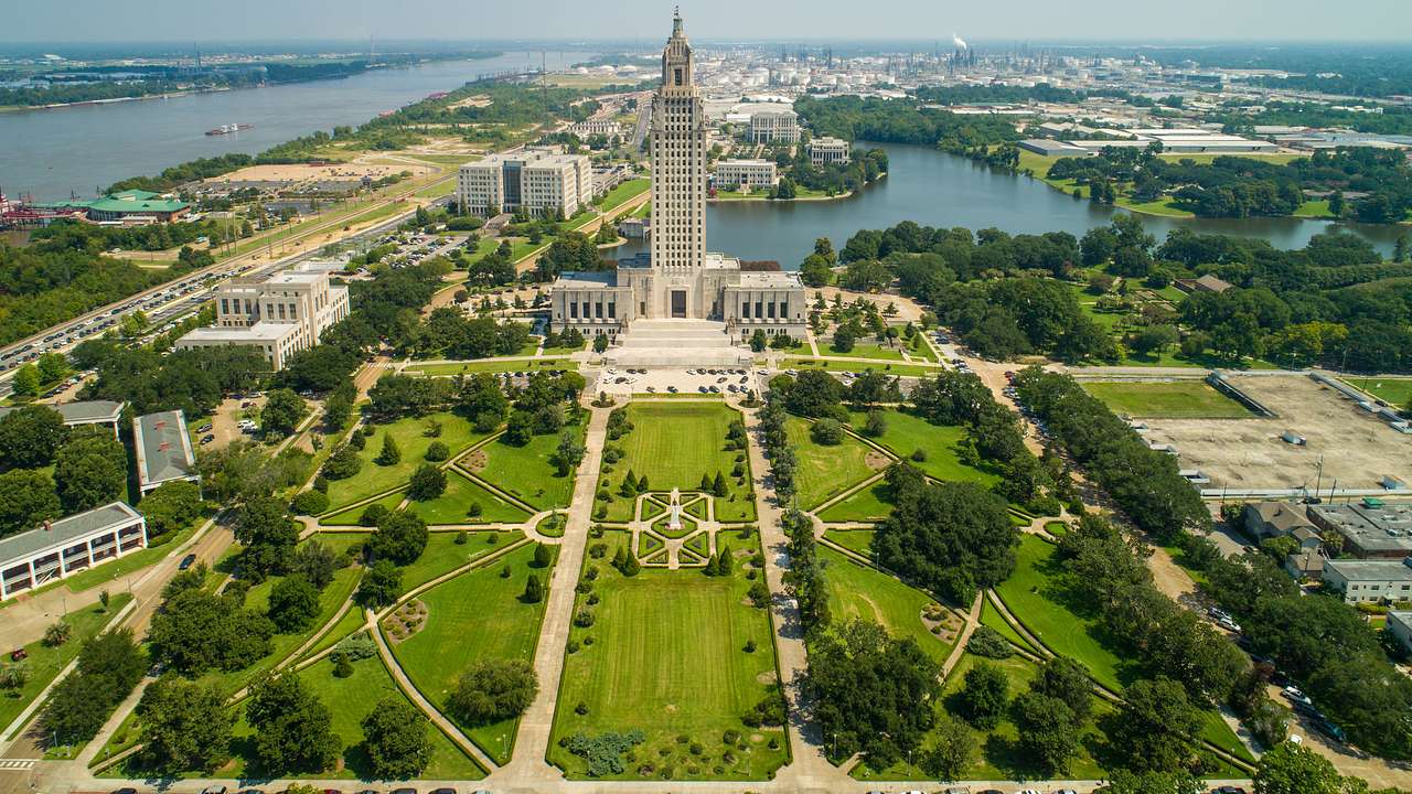 Aerial of a tall art-deco capitol building surrounded by lush greenery, on a nice day