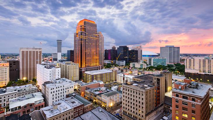 A downtown skyline of lit-up buildings under a cloudy evening sky